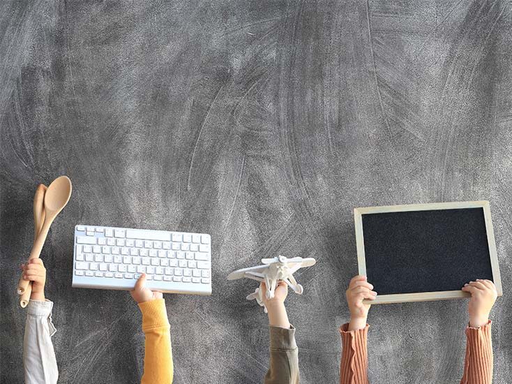 Foto zeigt Kinderhände mit Tafel, Flugzeug, Kochlöffel und Tastatur