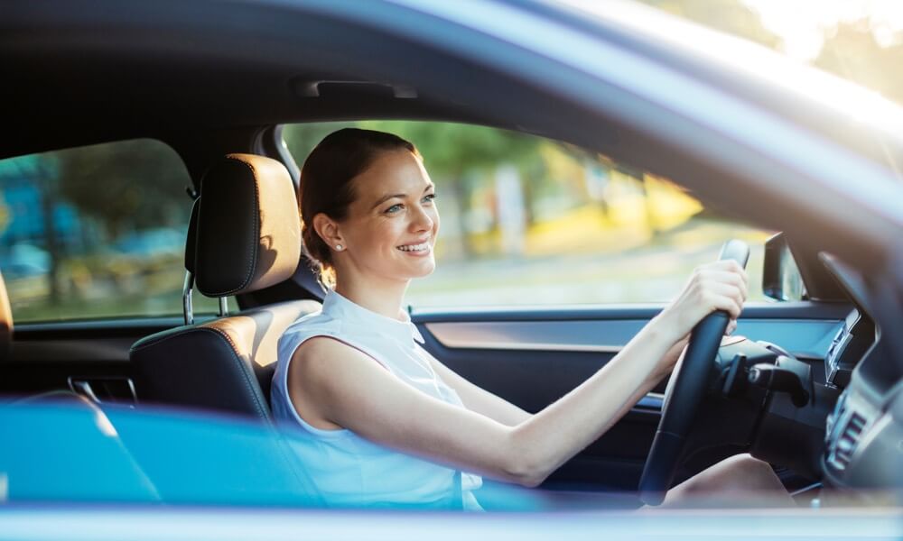 Frau sitzt lächelnd am Steuer ihres Autos.