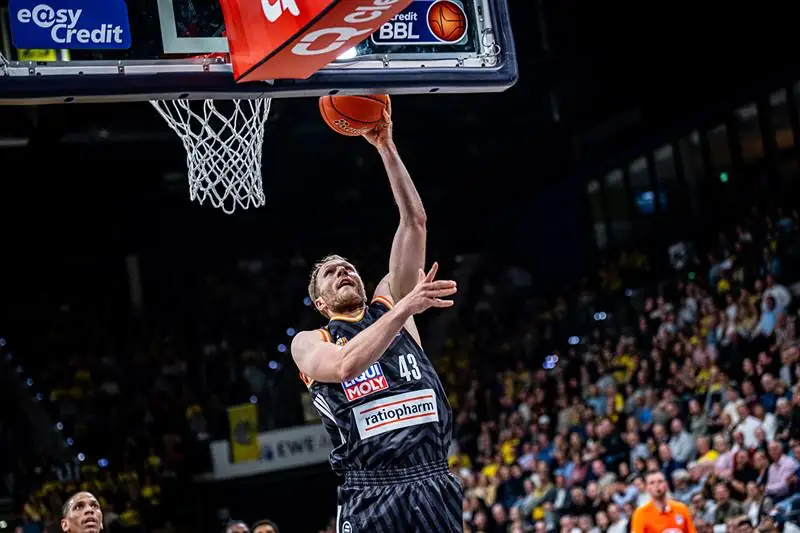 Spieler mit Basketball in der Hand springt zum Korb hoch und macht einen Dunk. 