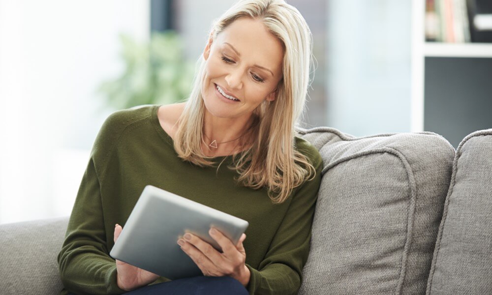 Frau sitzt mit ihrem Tablet auf dem Sofa.