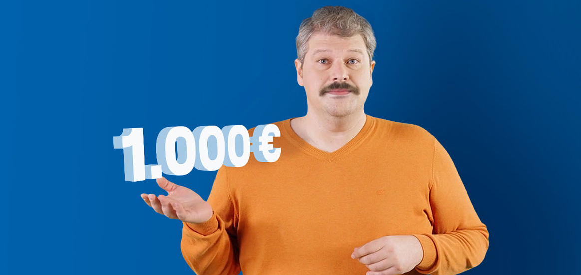Siggi steht in einem orangenem Pullover vor einer blauen Wand. Der Betrag 1000€ schwebt über seiner Hand.