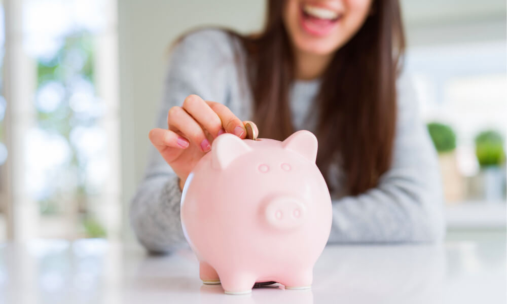 Eine Frau steckt lächelnd eine Münze in ein Sparschwein