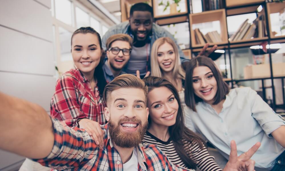 7 junge Leute sind lachend zu einem Gruppenselfi positioniert.