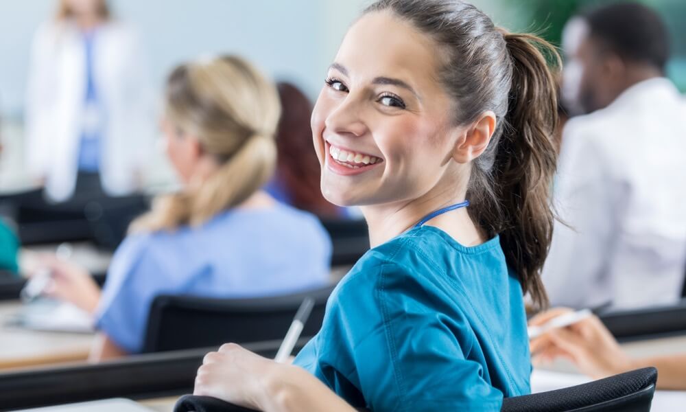 Studentin sitzt im Hörsaal und blickt lächelnd über ihre Schulter.