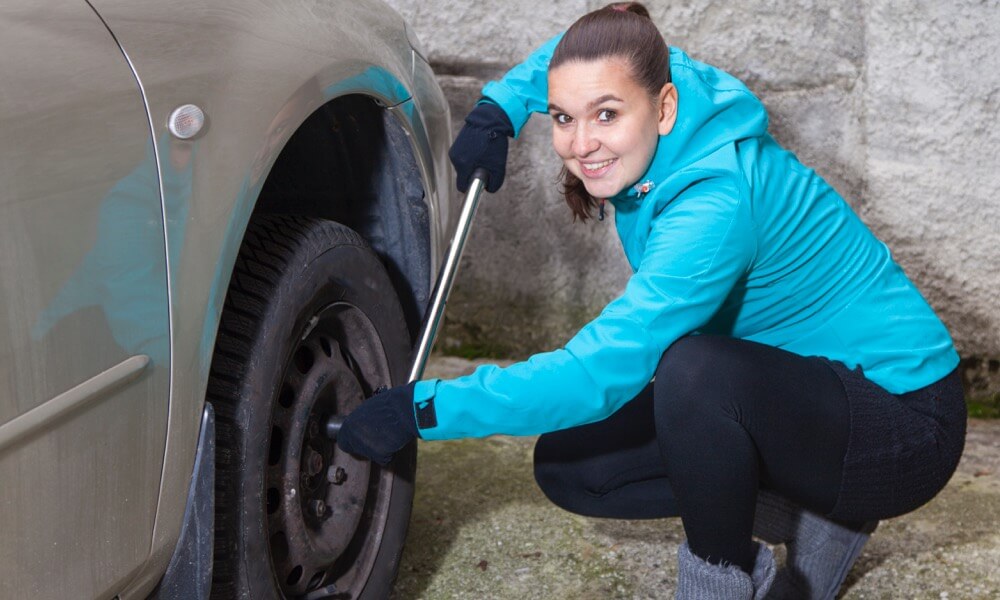 Frau hockt neben einem Auto zum Wechseln der Autoreifen