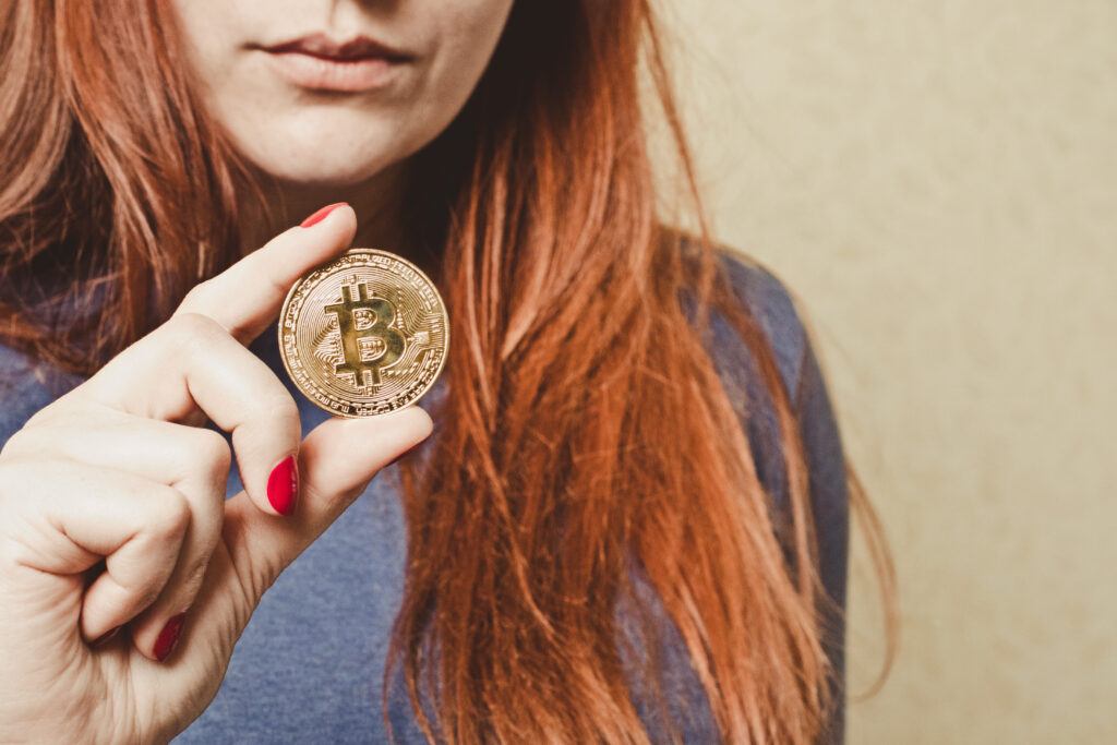 Eine rothaarige Frau hält eine Bitcoin Münze in ihrer Hand