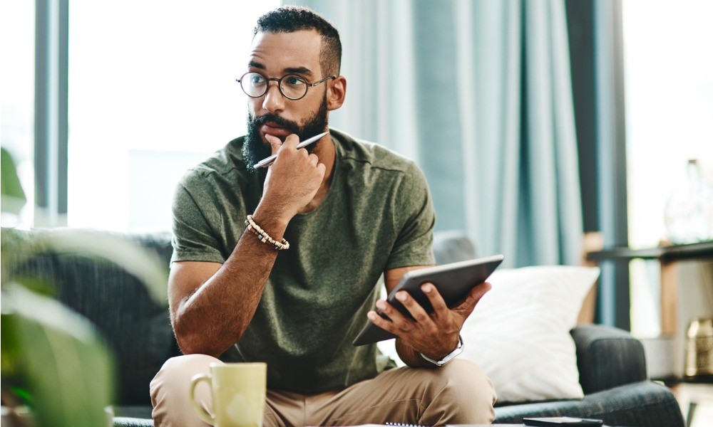 Ein Mann sitzt nachdenklich mit seinem Tablet in der Hand auf einem Sofa