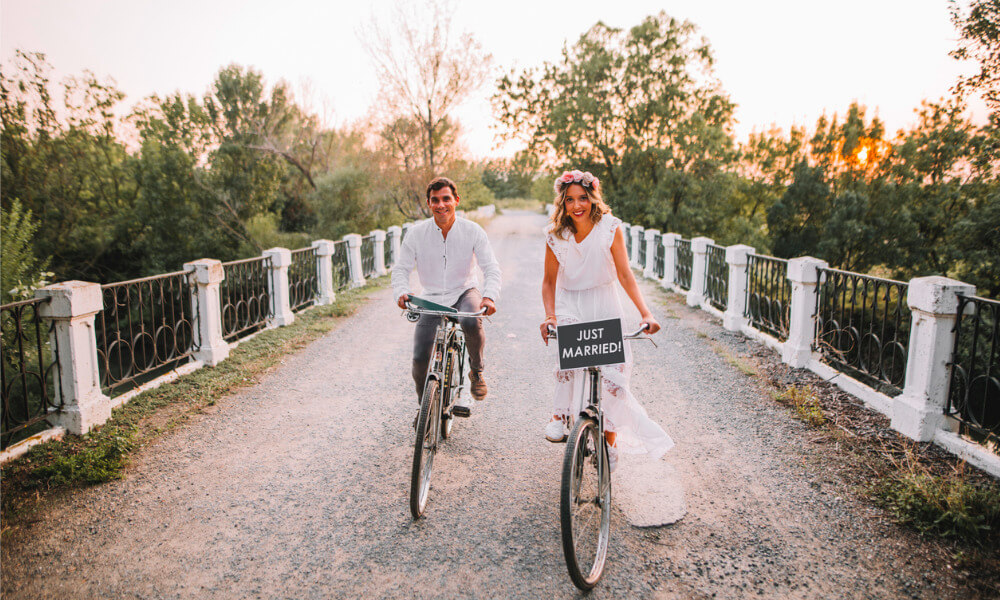 Ein frisch verheiratetes Brautpaar fährt mit Fahrrädern durchs Grüne.