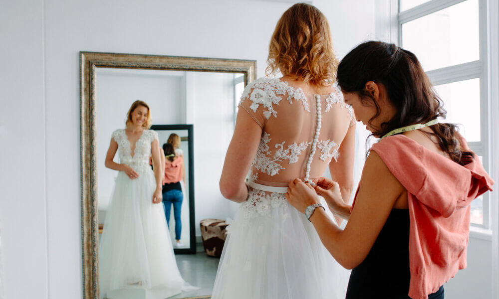Eine Braut probiert ein Brautkleid vor dem Spiegel an.
