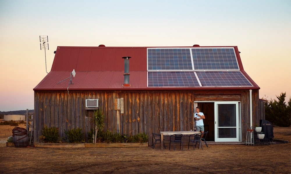 Ein Mann lehnt an der Wand eines Holzhauses mit installierter Photovoltaik-Anlage