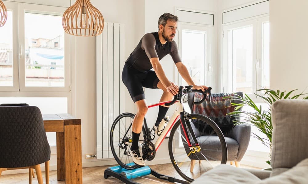 Mann trainiert in seinem Wohnzimmer mit Fahrrad auf dem Rollentrainer.