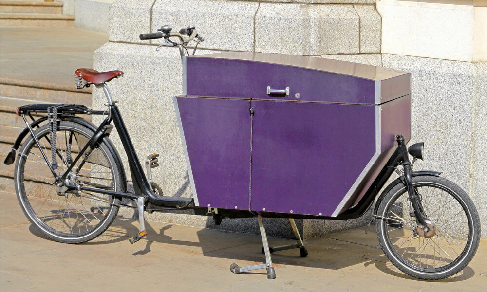 Ein einspuriges Lastenrad mit großer violetter Transportbox.