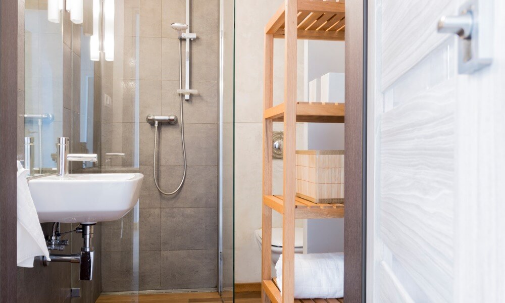 Ein schmales Badezimmer mit grau gefliesten Wänden und einem dunklen Laminatboden.